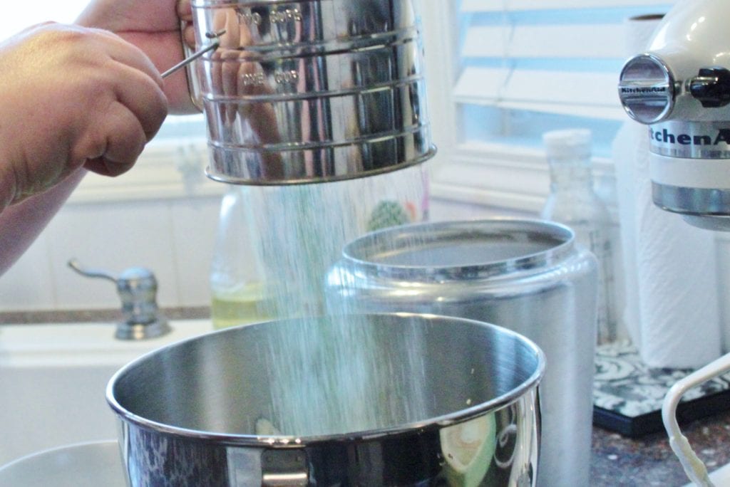 A baker sifting matcha into a mixer bowl
