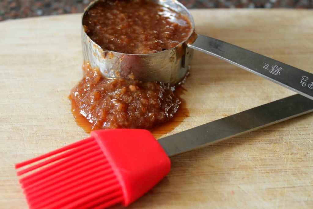 A measuring cup full of brown chunky barbecue sauce and a red brush. 