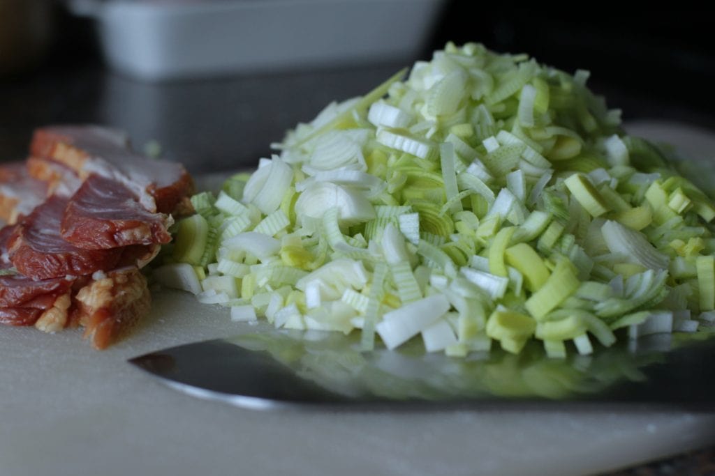 A pile of chopped leeks beside slices of bacon.