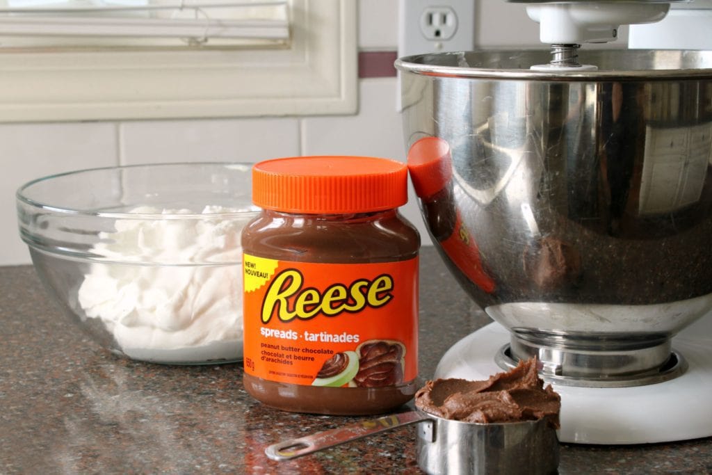 A jar of Reese's Chocolate Peanut Butter spread sits in front of a bowl of whipped cream.