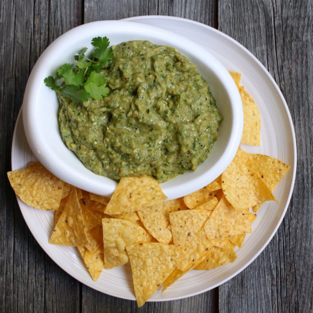 A Bowl of chunky green dip and some chips on the side