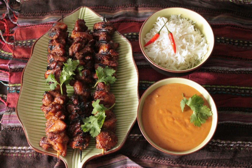 A platter of grilled Thai Chicken Satay beside a bowl of rice and satay dipping sauce.