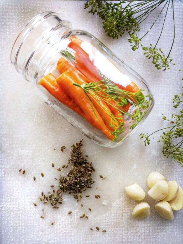 Pickled Carrots with Dill and Garlic - A half packed jar of bright carrots, fresh dill, and garlic surrounded by more fresh dill and garlic.