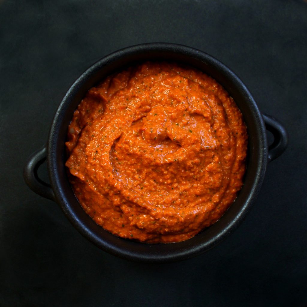 Romesco Sauce - A bright orange sauce in a black bowl against a black background. 